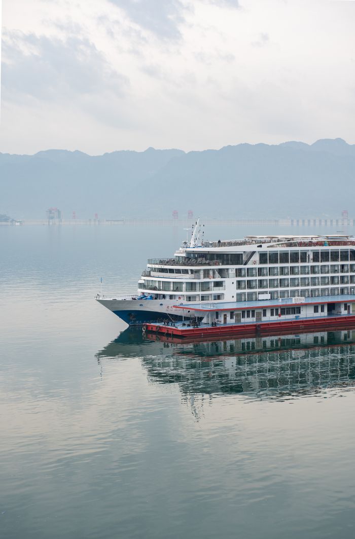 Luxury cruise ship navigating serene waters with mountain backdrop.